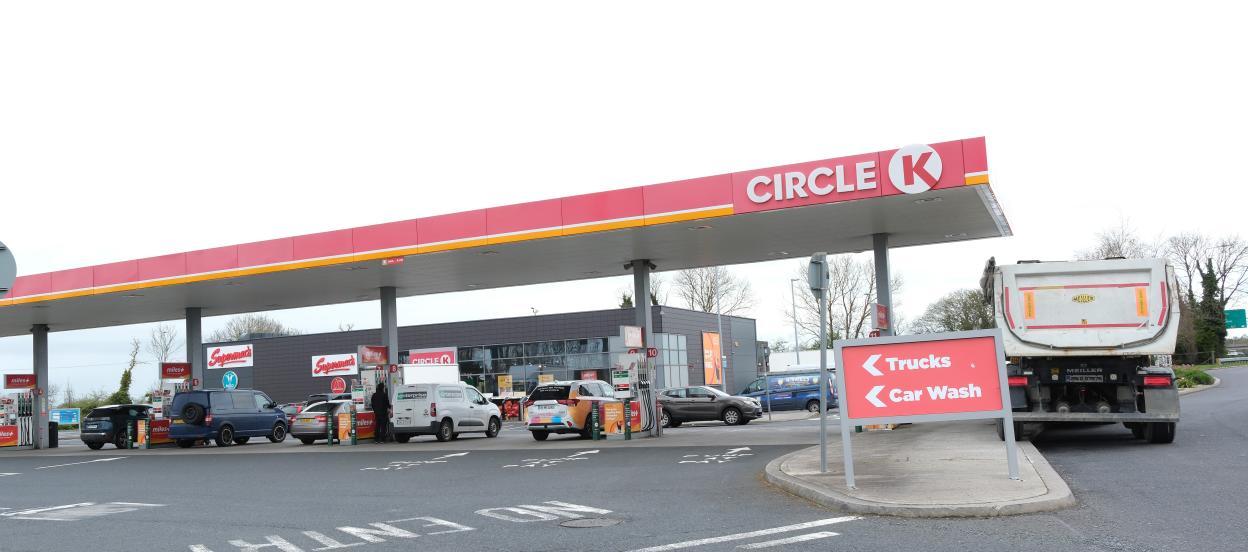 Cars and vans at pumps under a Circle K gas station canopy, with a sign for trucks and car wash.