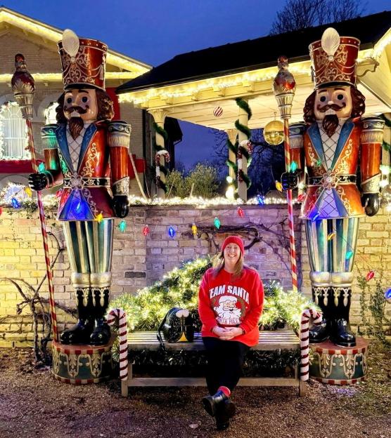 A woman in a red "Team Santa" sweater sitting on a bench between two large nutcracker statues.