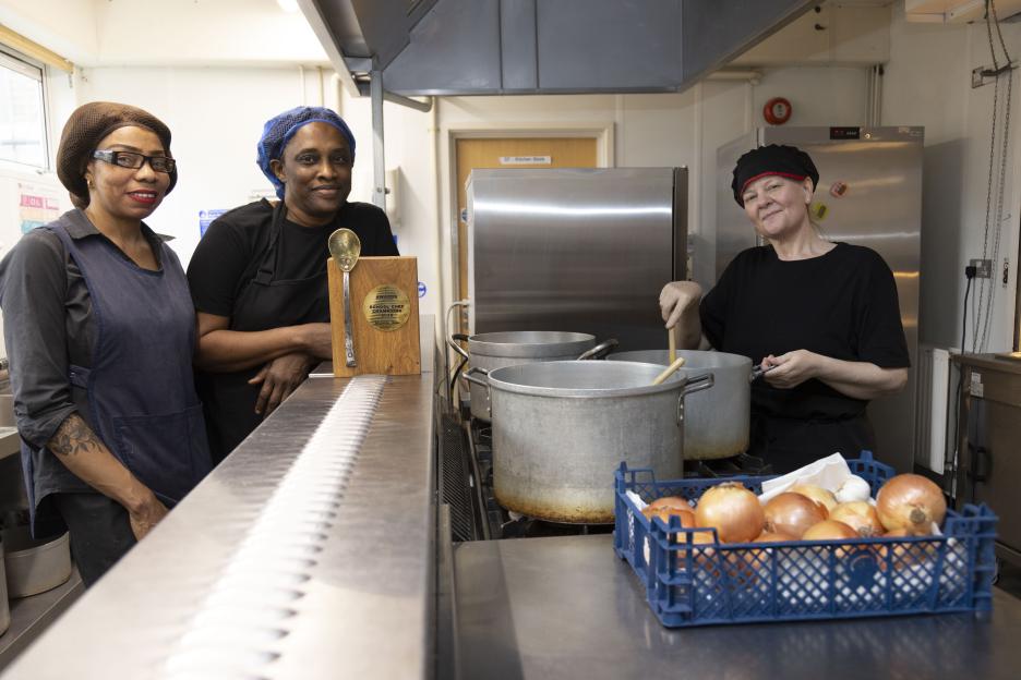 Tracey Nwabia and her two assistants, Abi and Stella, in a kitchen, with Tracey holding an award.