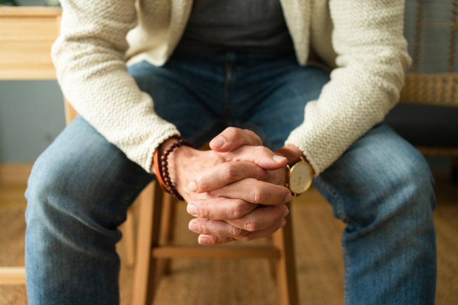 Unrecognizable man with hands clasped in living room. Close-up