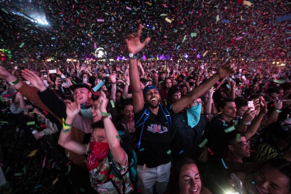 Confetti falls on a crowd of people with their hands raised at a concert.