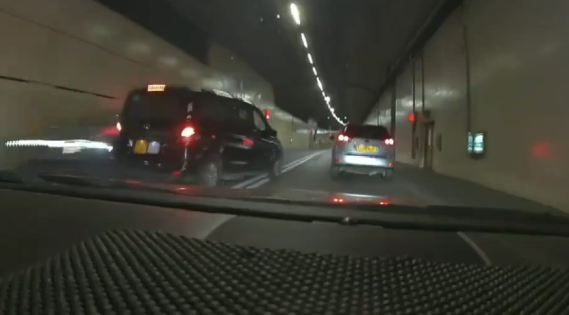 A black van and a silver car driving in a tunnel from a dashcam perspective.