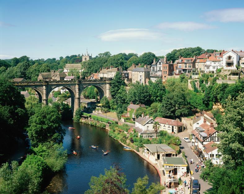 Knaresborough with boats on River Nidd below a stone arch bridge and buildings on either side.
