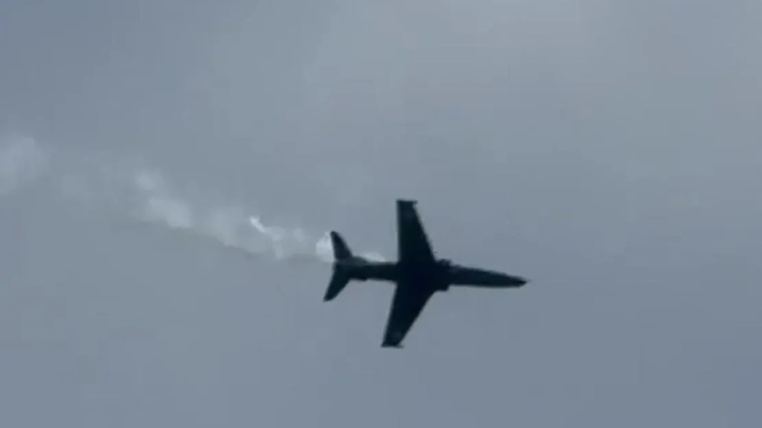 A Hawk T2 training aircraft flying against an overcast sky, leaving a trail of white smoke.