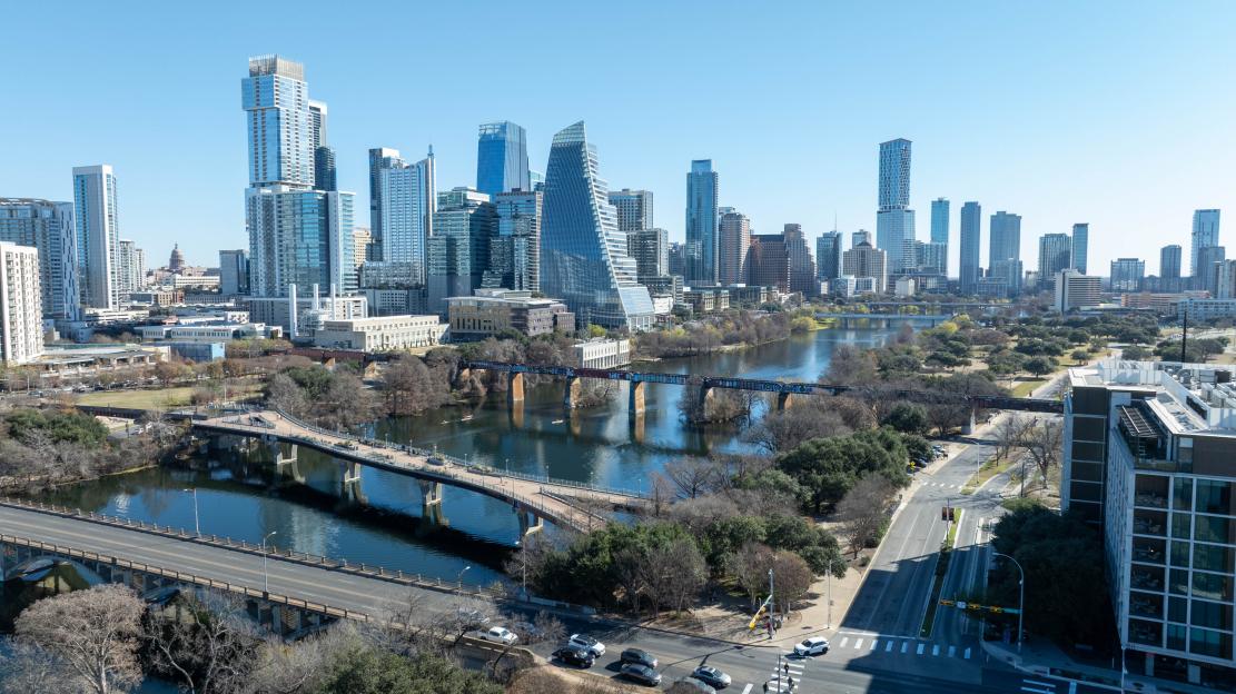 Aerial view of the Austin, Texas skyline, with a river and bridges in the foreground.