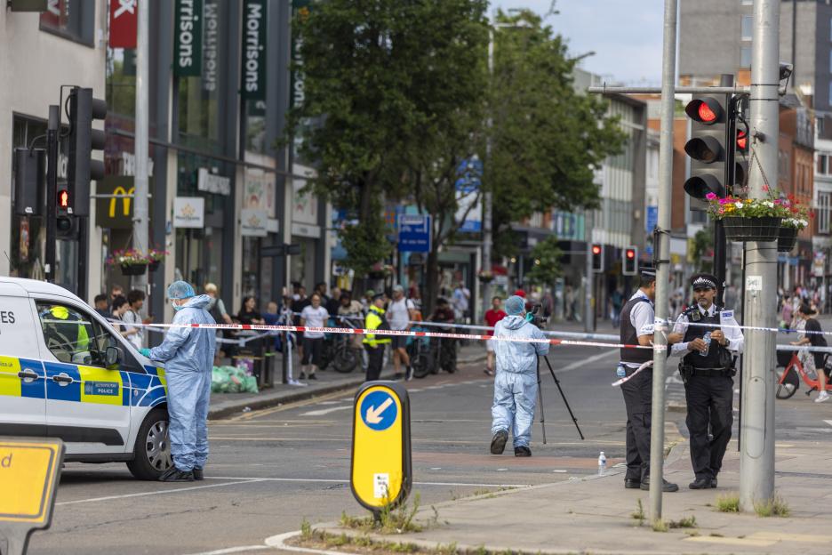 Forensic police officers in blue protective suits gather evidence at the scene of a car crash in Ealing Broadway, London.