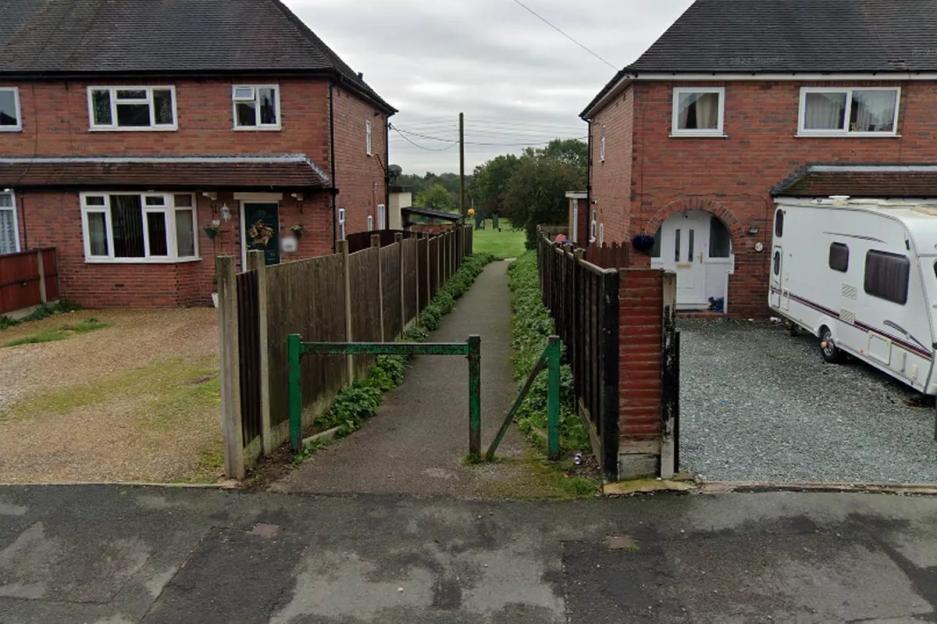 An alleyway with a green barrier between two brick houses.