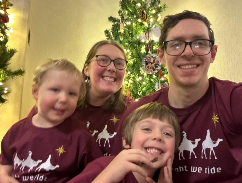 Greer Jones, her husband Chris, and their sons Zeke and Zac, smiling in matching shirts in front of a Christmas tree.
