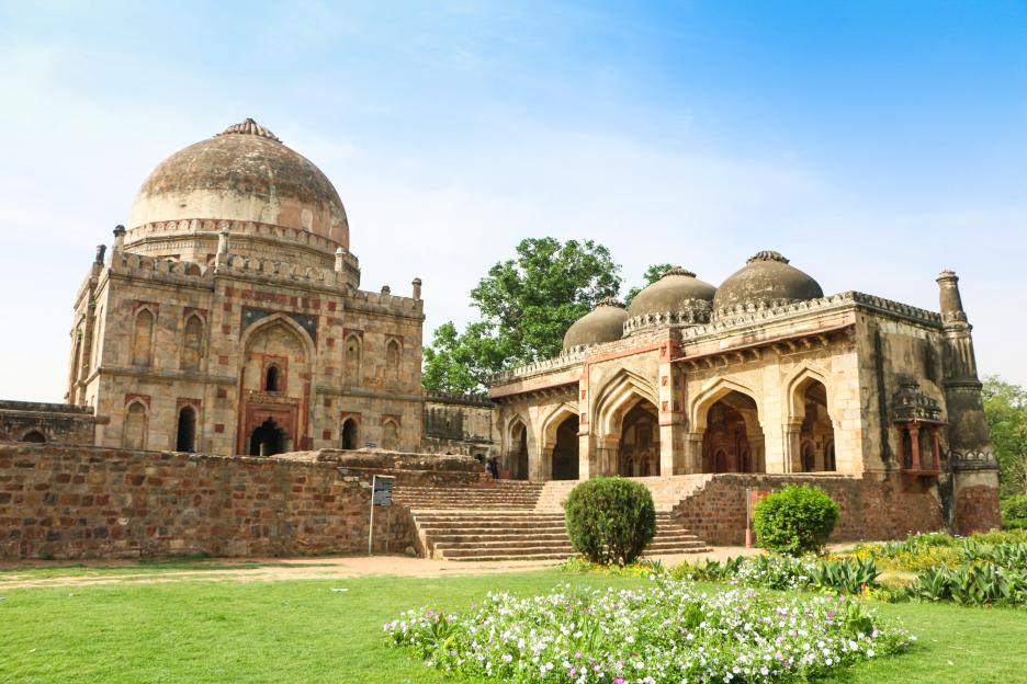 Lodhi Garden in New Delhi, India, featuring ancient monuments including a mosque and a dome-topped structure, surrounded by green grass and flowers.