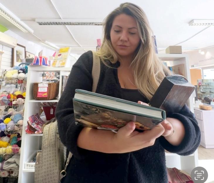 Jessica Apps shopping at a charity shop, holding two books.