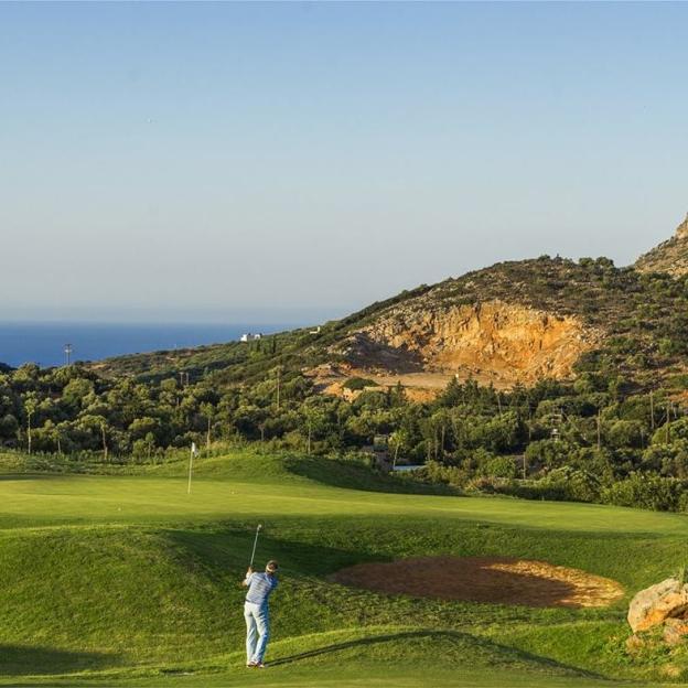 A golfer on the Crete Golf Club course in Hersonissos, with the Mediterranean Sea and hills in the background.