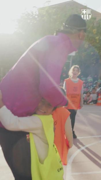 A woman in a magenta top embracing a child in a yellow bib, with another child in an orange bib and several more children in the background.