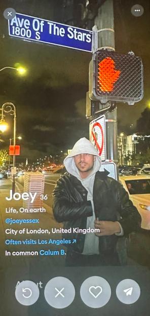 A mobile phone displaying a dating app profile for Joey, 36, from London, United Kingdom, showing a photo of him in a black leather jacket and gray hoodie on a street at night.