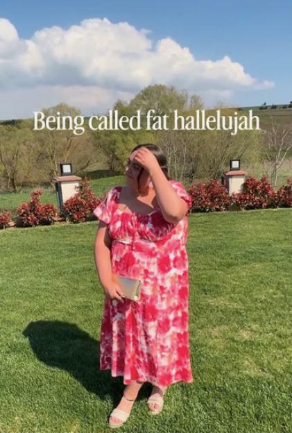 Woman in a red and white floral dress standing outdoors, with text "Being called fat hallelujah" overlaid.