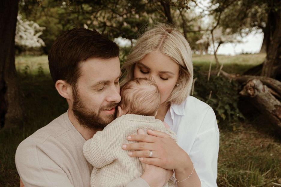 Dan Kettle and wife Bethan holding baby Rex under a tree.