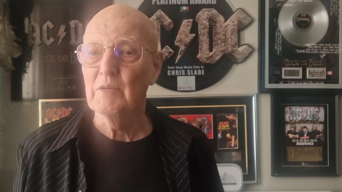 AC/DC drummer Chris Slade in front of several framed AC/DC awards and memorabilia.