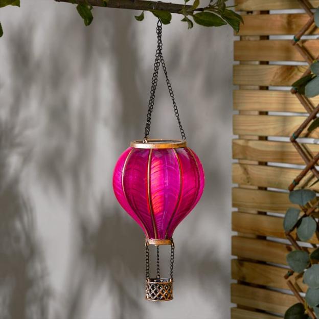 A pink hot air balloon light with a bronze frame hangs from a tree branch.