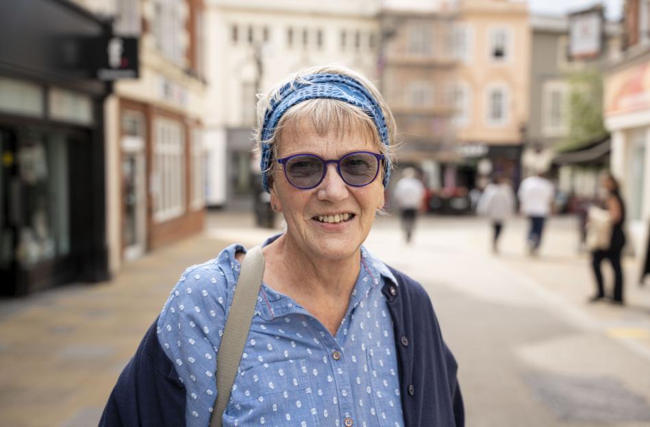 A smiling woman wearing blue-tinted glasses and a blue polka-dotted shirt over a navy cardigan.