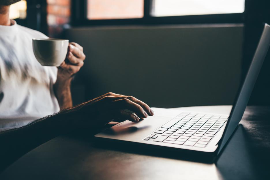 A man drinks coffee while using a laptop at home.