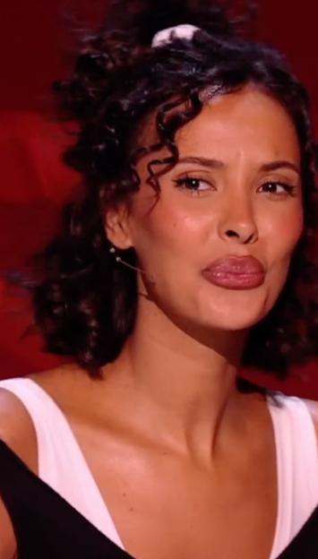 A woman with curly brown hair and plump lips wearing a white and black top.