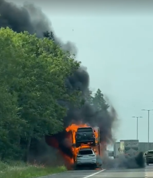 A car carrier truck with vehicles on fire on a highway.