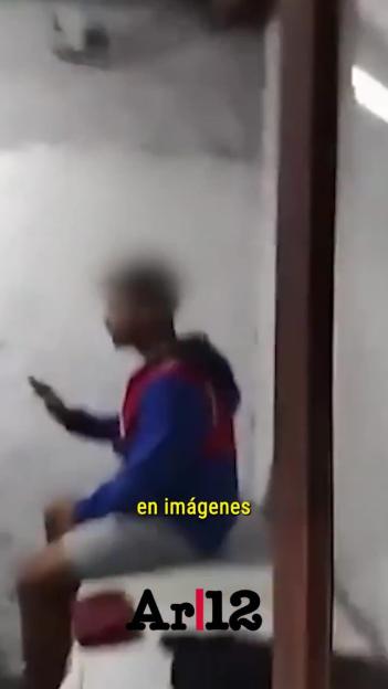 Blurry image of a person sitting, wearing a blue and red top and white shorts, looking at a phone, with text "en imágenes" and "Ar|12".