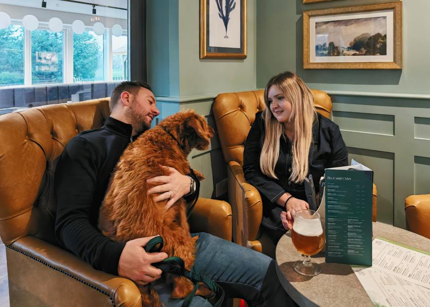 A man petting his dog while sitting across from a woman at a table.