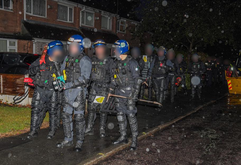 Police officers in tactical gear preparing for an early morning raid.