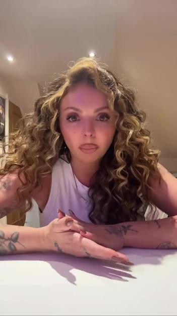 Jesy Nelson with curly hair, wearing a white top, looking directly at the camera.