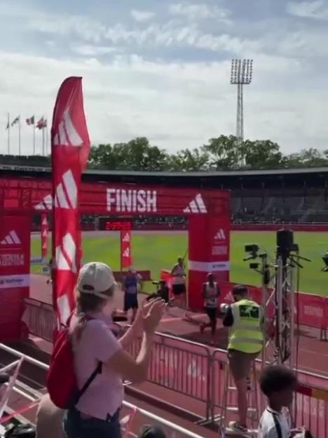 A woman in a white hat claps at runners crossing the finish line of a race.