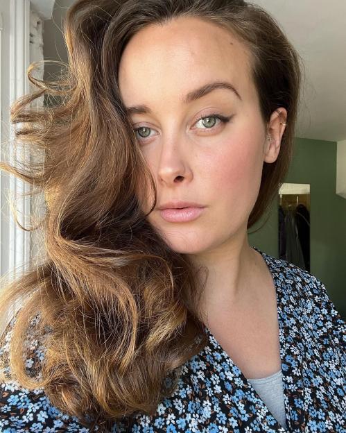 A woman with long wavy brown hair and green eyes looks directly at the camera.