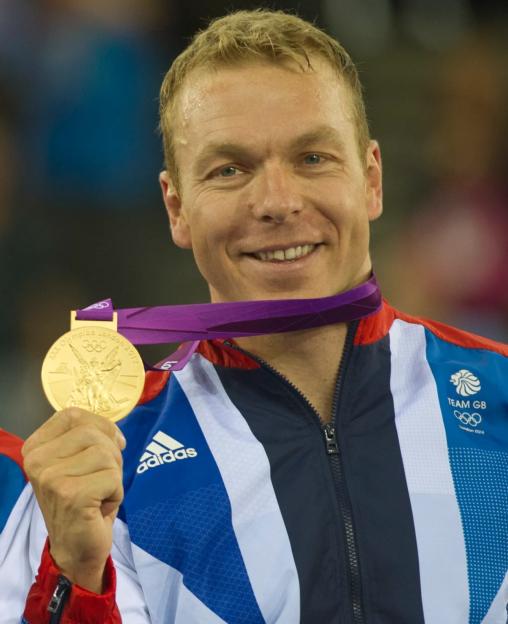 Chris Hoy, wearing his Team GB jacket, holding up his gold medal from the London 2012 Olympics.