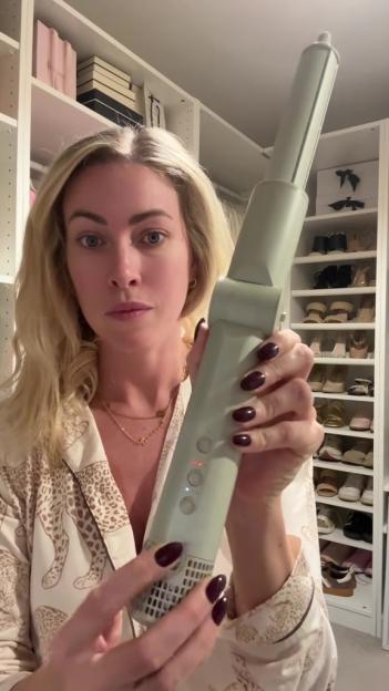 A woman holding a light green hair styling tool.