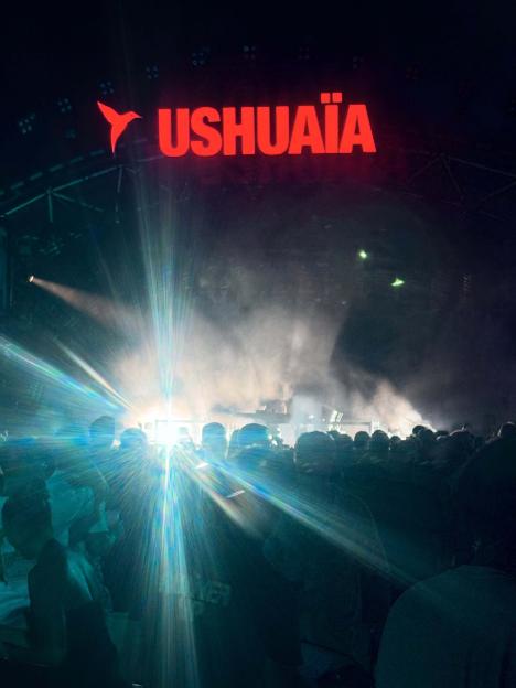 Nighttime photo of a stage with "USHUAÏA" lit in red, above a crowd of people and bright stage lights.