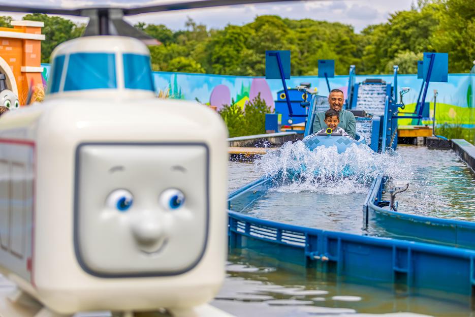A father and child on a log flume ride creating a big splash, with a Thomas the Tank Engine character in the foreground.