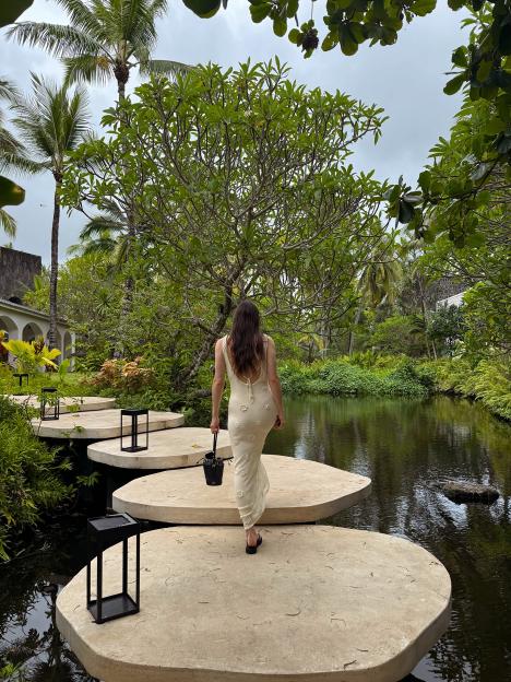A woman in a cream dress walks across stepping stones over a pond.