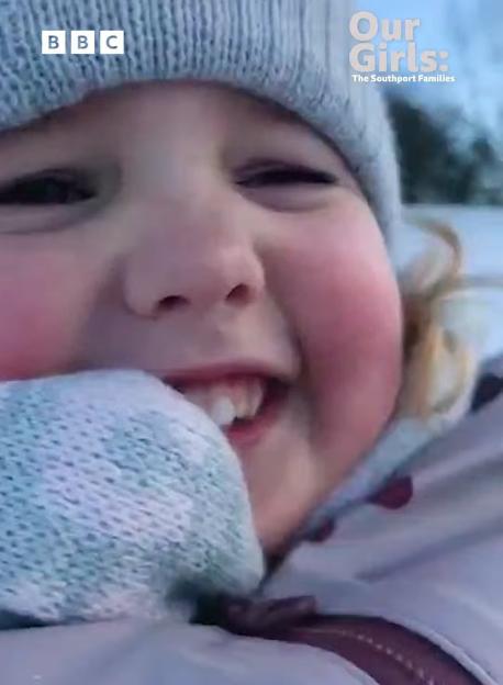 A smiling child in a winter hat and coat, wearing mittens, with text "Our Girls: The Southport Families" and BBC broadcast information.
