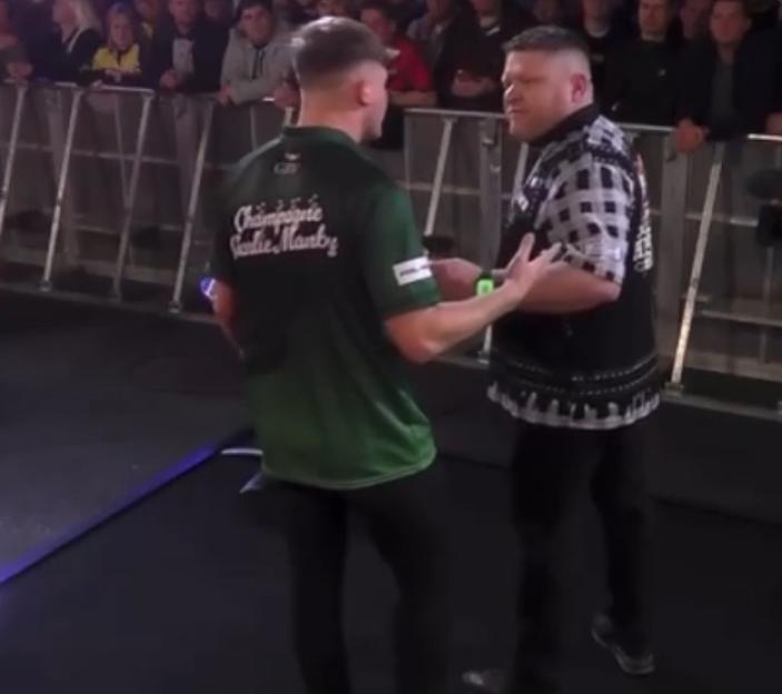 Two male athletes facing each other, one in a green shirt and one in a black and white patterned shirt, on a sports stage.