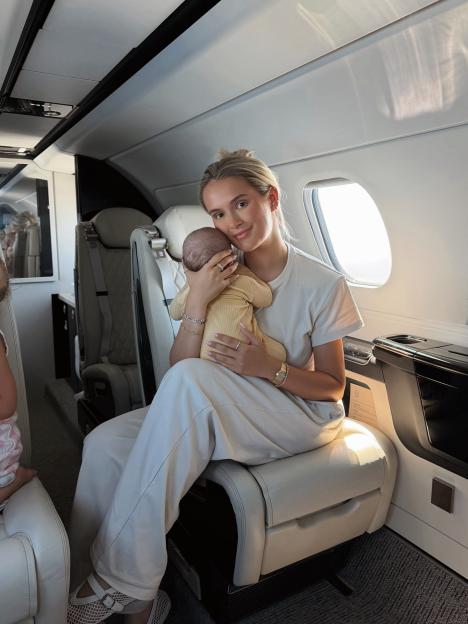 A woman holding a baby while sitting in a private jet.