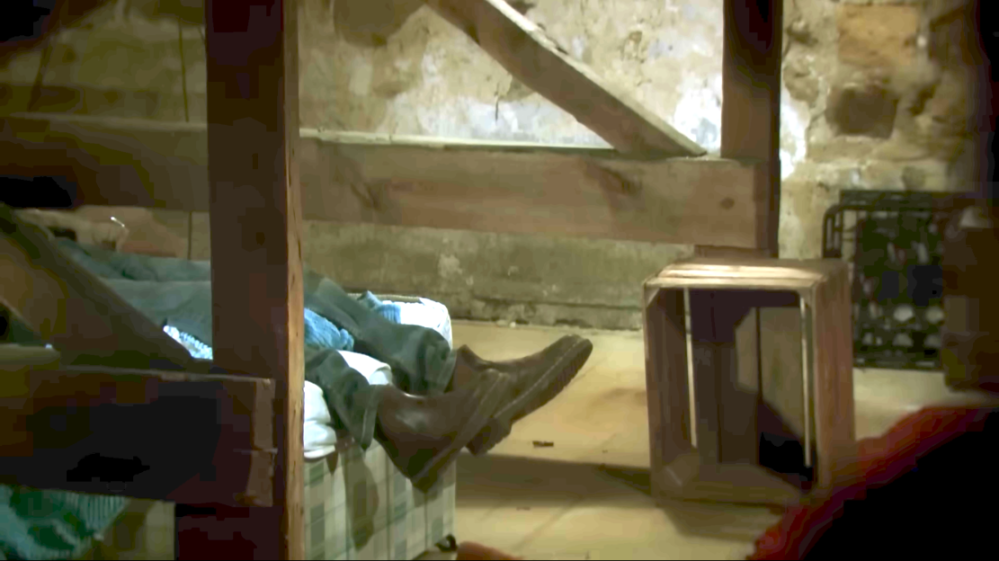 Person wearing shoes on a bed in a rustic room.
