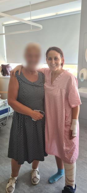 Annie Perez, with a bandaged arm and leg from severe burns, standing next to a friend in a hospital.