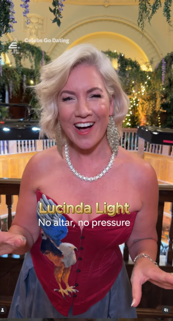 Lucinda Light from Celebs Go Dating, wearing a red corset with an eagle, smiling with her mouth open.