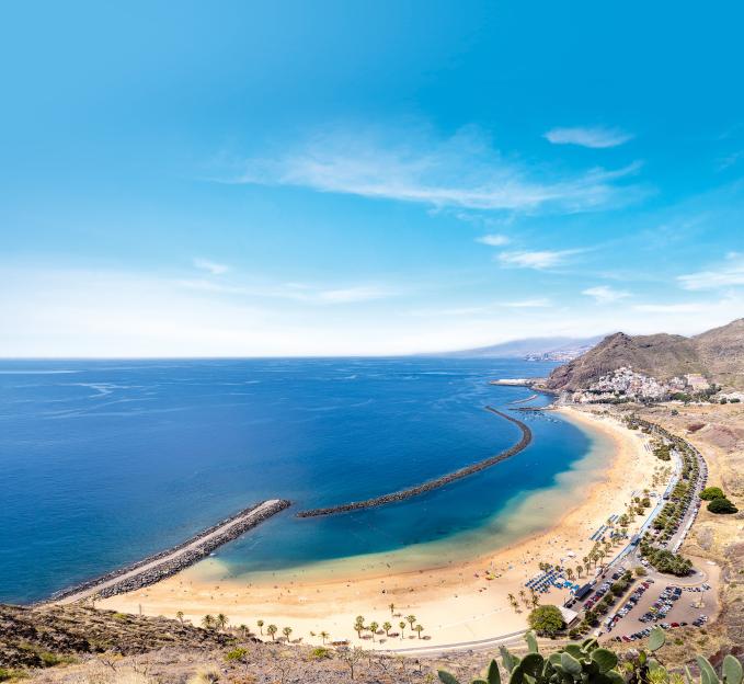 Panoramic view of Las Teresitas beach in Tenerife, with clear blue water, a sandy beach, and a distant town.