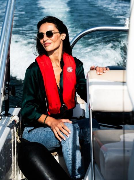 A woman in sunglasses and a red life vest smiles while sitting on a boat.