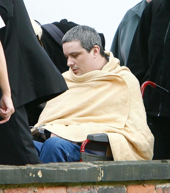 Ian Huntley, wrapped in a blanket, sits in a wheelchair with his wrists handcuffed.
