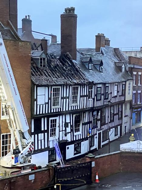 A historic 16th-century half-timbered building with significant fire damage to its roof, with a fire truck ladder extended towards the building.