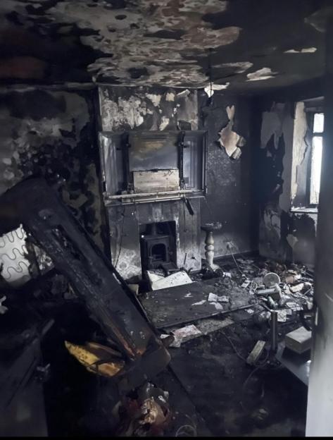 The remains of a room damaged by a house fire, showing charred walls, ceiling, and debris.