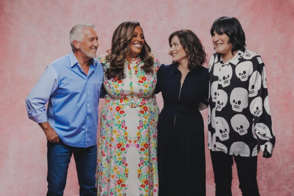 The Great British Bake Off judges and hosts smiling.