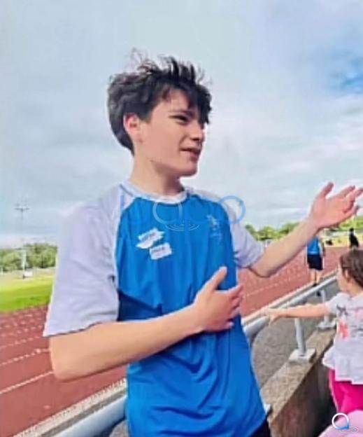 A boy in a blue and white shirt gestures with his hands on a running track.