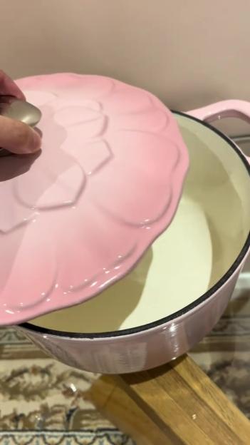 A hand lifting the floral lid off a pink Dutch oven.